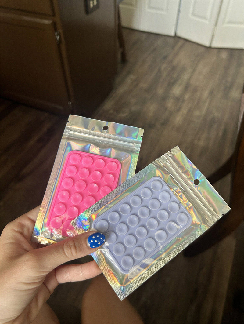 Support téléphone à ventouses rose et lilas dans leur sachet holographique, tenus en main